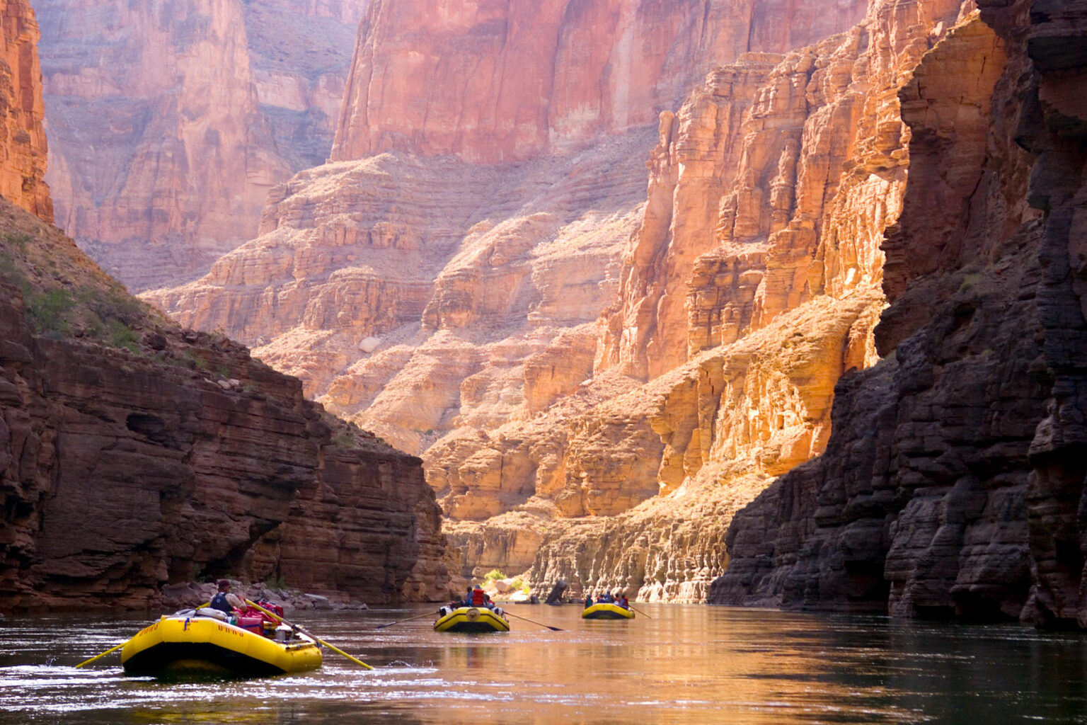 OARS rafts follow in a line through brightly lit canyon at heart of Grand Canyon