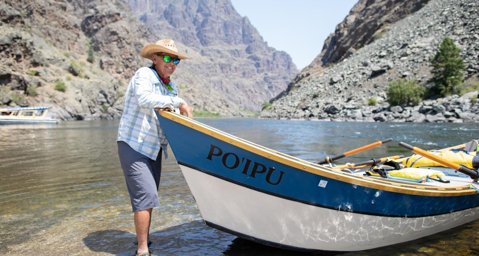 Legendary Idaho river guide Curt Chang stands knee-deep in the Snake River next to his blue and white dory, Poi’pu.