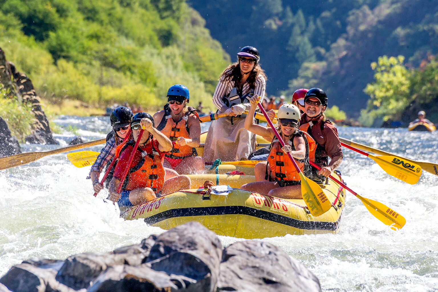Guide qnd guests smile for the camera as they paddle their oar-assisted paddle raft through rapids on the Rogue River