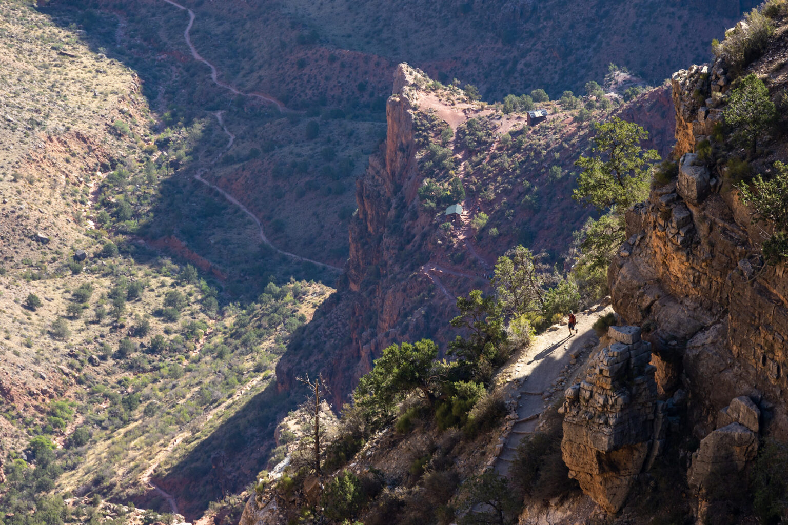 Lone hiker in sunlight along an otherwise shaded section of the Bright Angel Trail in Grand Canyon