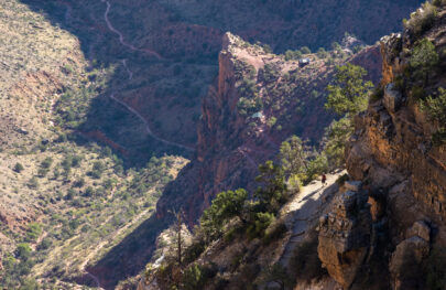 Lone hiker in sunlight along an otherwise shaded section of the Bright Angel Trail in Grand Canyon