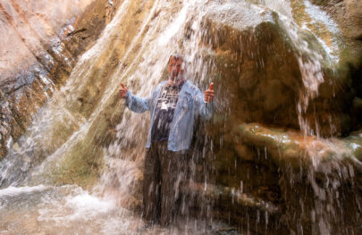 Man stands under waterfall and gives thumbs up in Grand Canyon