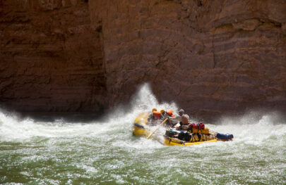 OARS raft hits rapid sending spray up in contrast to dark canyon walls