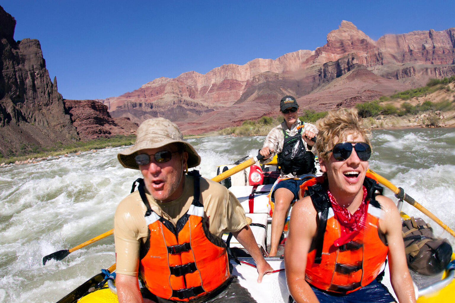 Father and son laughing as guide steers raft through whitewater in Grand Canyon