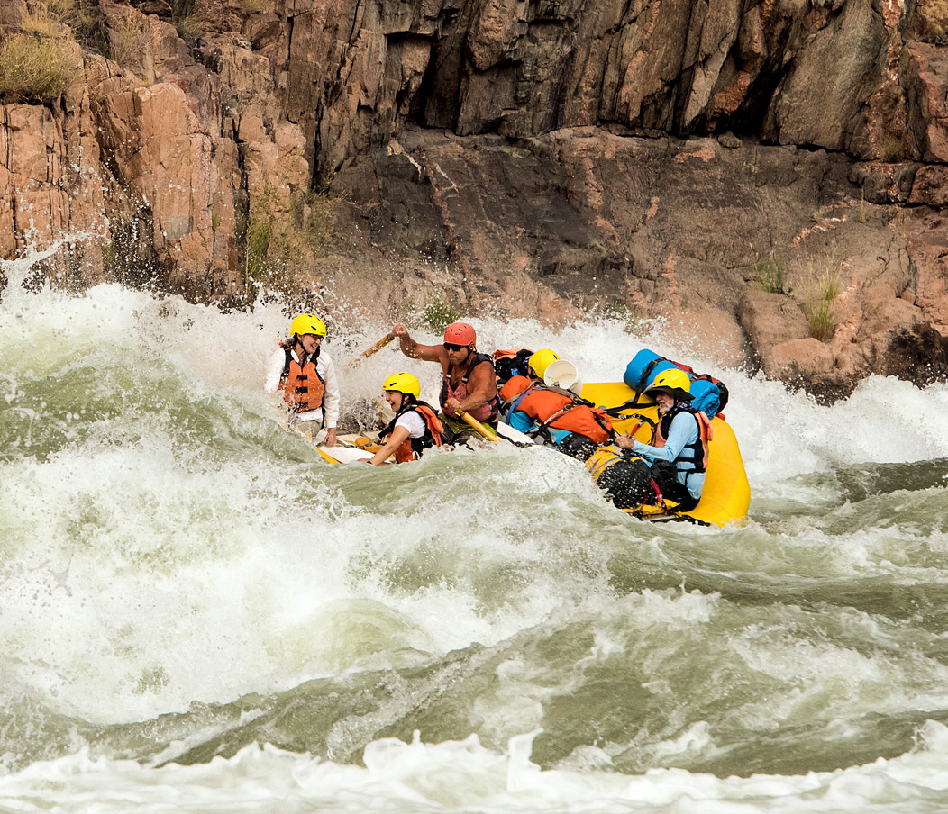 Guide navigates OARS raft through big water with smiling guests in Grand Canyon