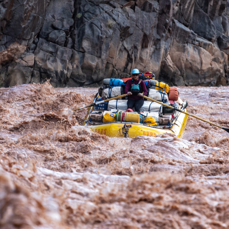 OARS baggage raft navigating muddy rapids in Grand Canyon.