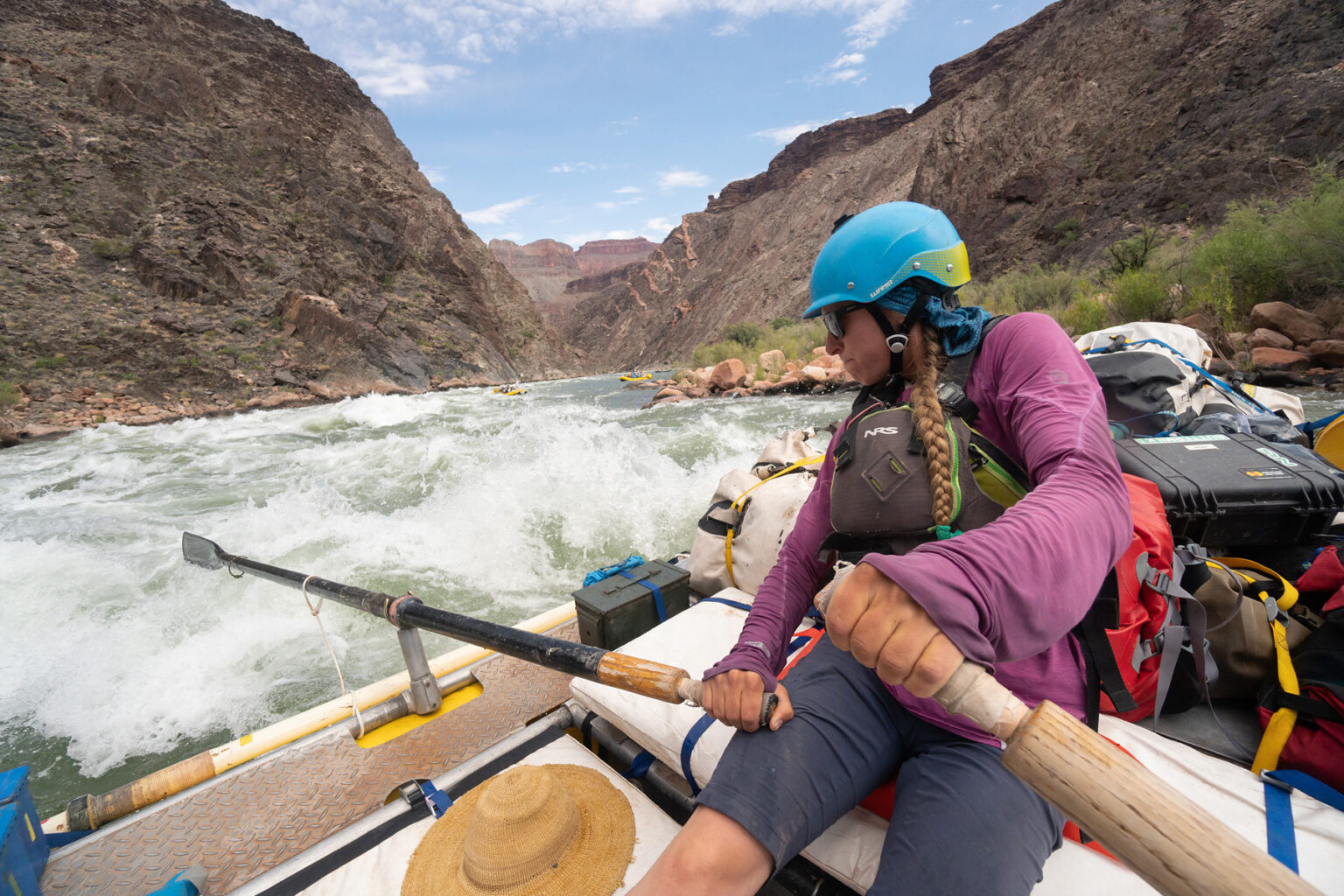 OARS guide in purple top and blue helmet rows her raft through big rapids in Grand Canyon
