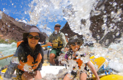 Splashy image of mother and daughter with guide at the oars as they navigate whitewater in Grand Canyon