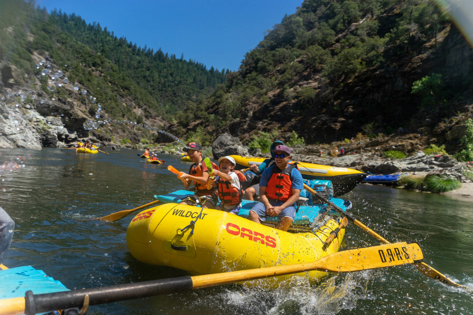 Family having fun with water guns while rafting on a river.