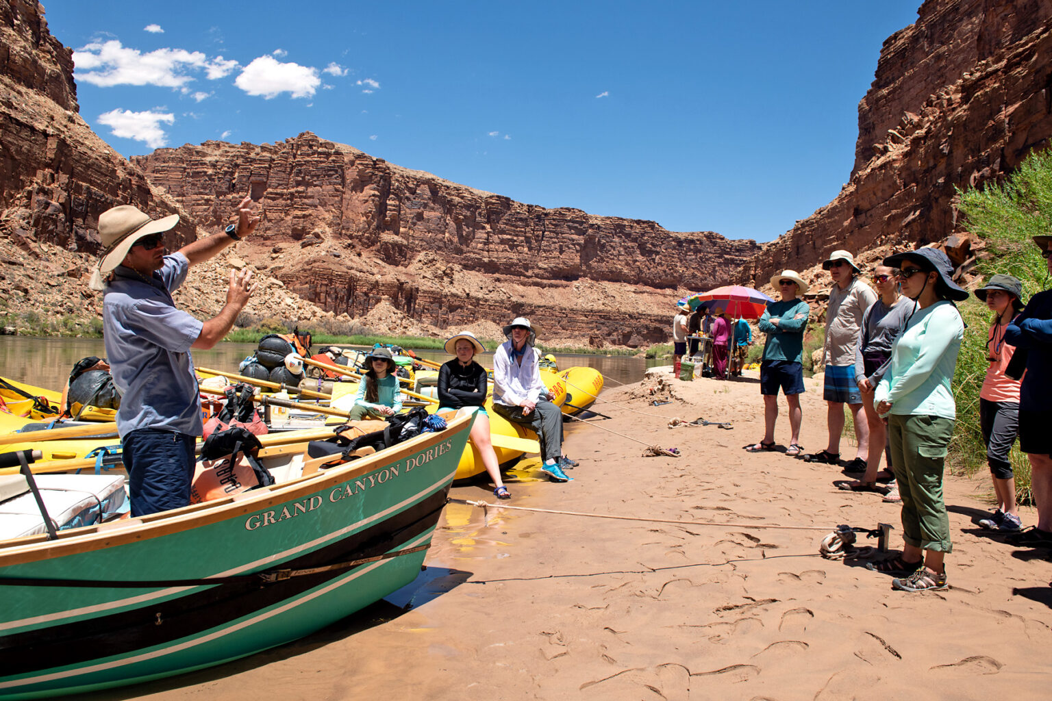 Lunch break on the banks of the Colorado River as OARS guide gives interpretive talk to guests from the bow of a Grand Canyon Dory
