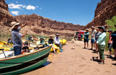 Lunch break on the banks of the Colorado River as OARS guide gives interpretive talk to guests from the bow of a Grand Canyon Dory