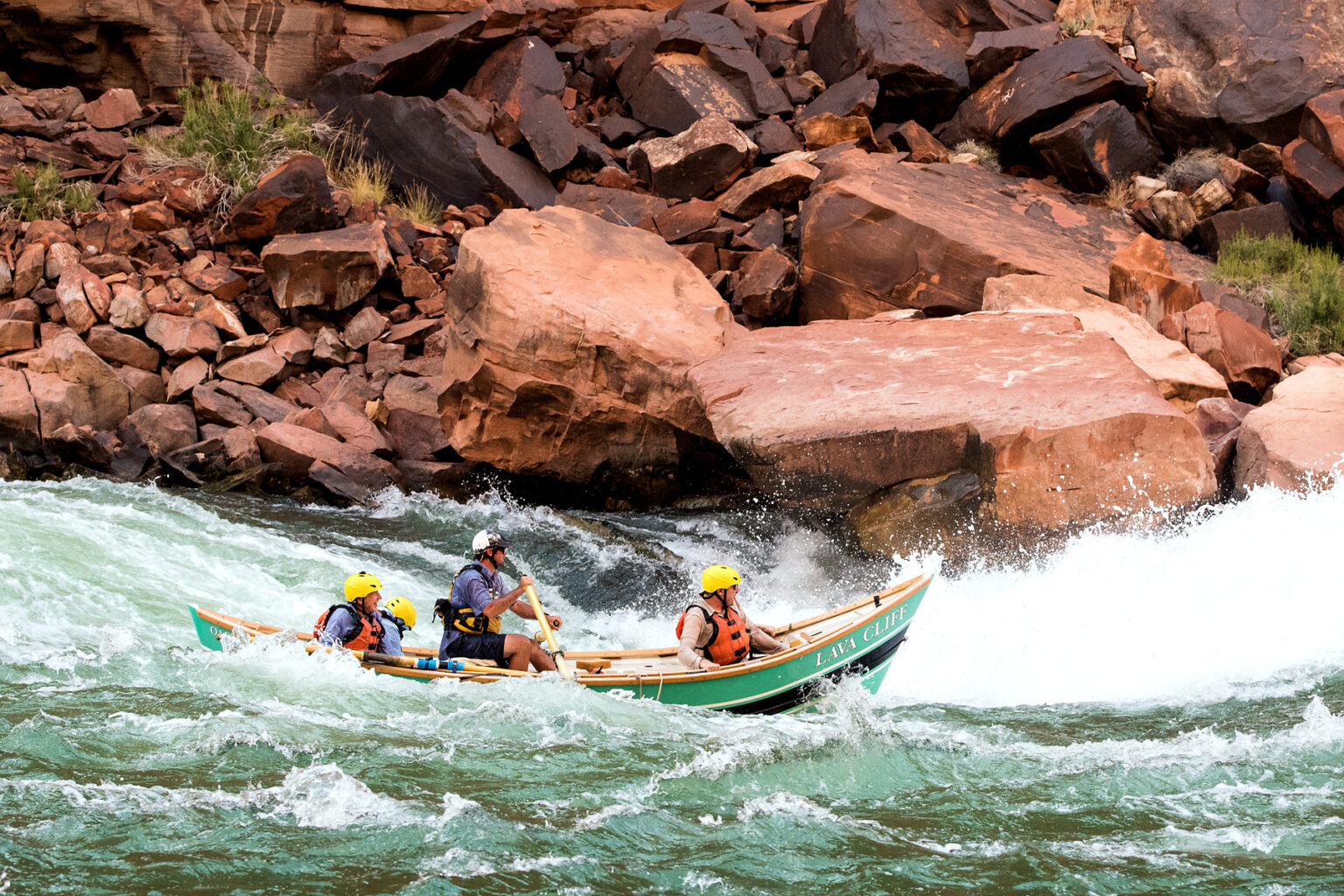 OARS Grand Canyon dory in the rapids with large boulders in the background