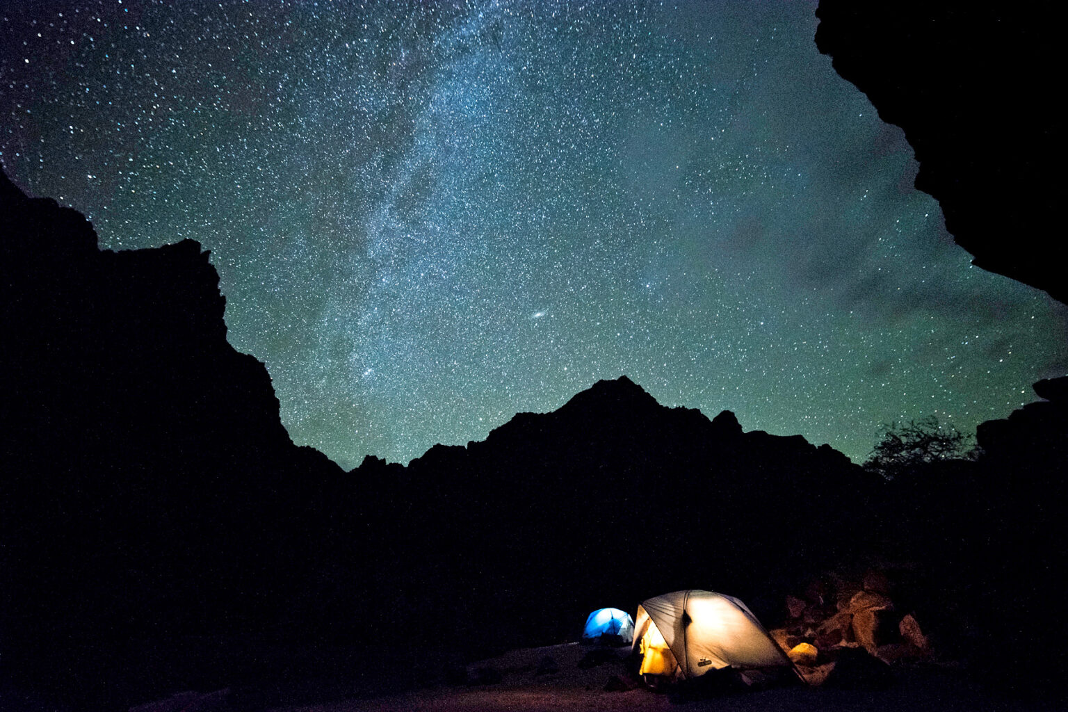 Night sky illuminated with brilliant stars and Milky Way with tent lit from inside in Grand Canyon