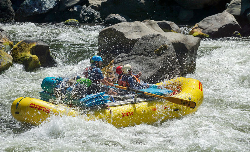 A river guide navigates an OARS raft through a rocky canyon on the Rogue River
