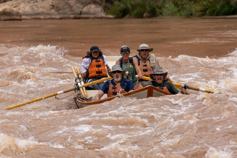 An OARS guide navigating the Colorado River with a boat full of guests