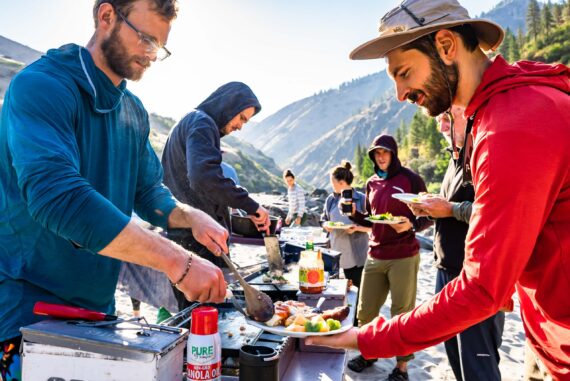 group of people serving themselves dinner from a table outside in the mountains.
