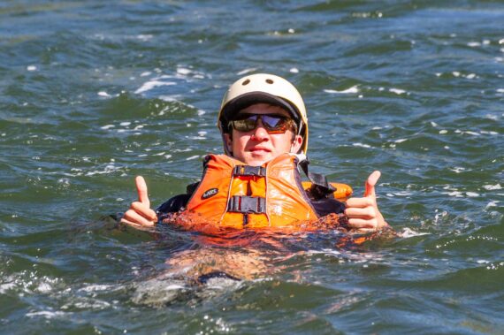 man floating in water in a life vest giving a thumbs up.